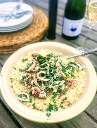 risotto in serving bowl topped with squid and herbs next to bottle of champagne