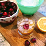 old-fashioned cocktail next to cherries and oranges